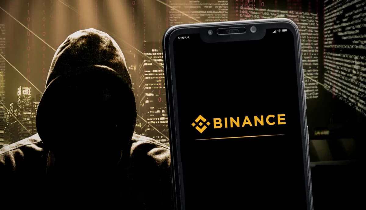 homem com capuz ao lado de celular com logo da binance criptomoedas