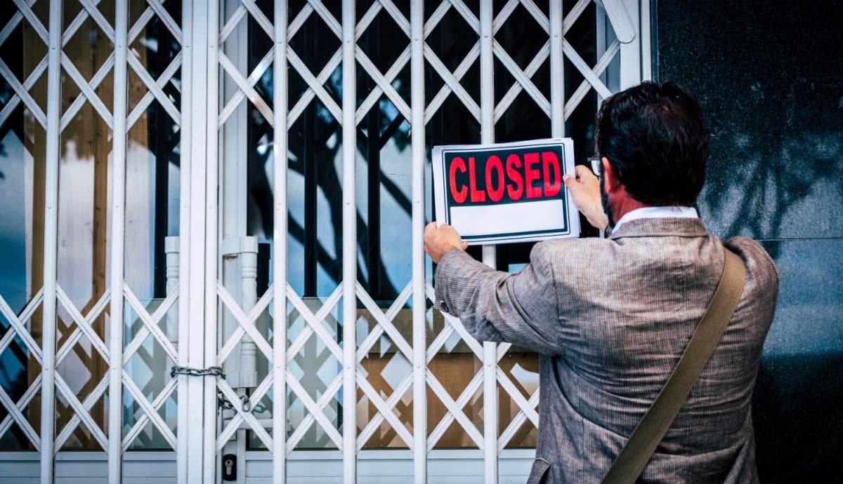 homem com placa de fechado closed em frente a loja